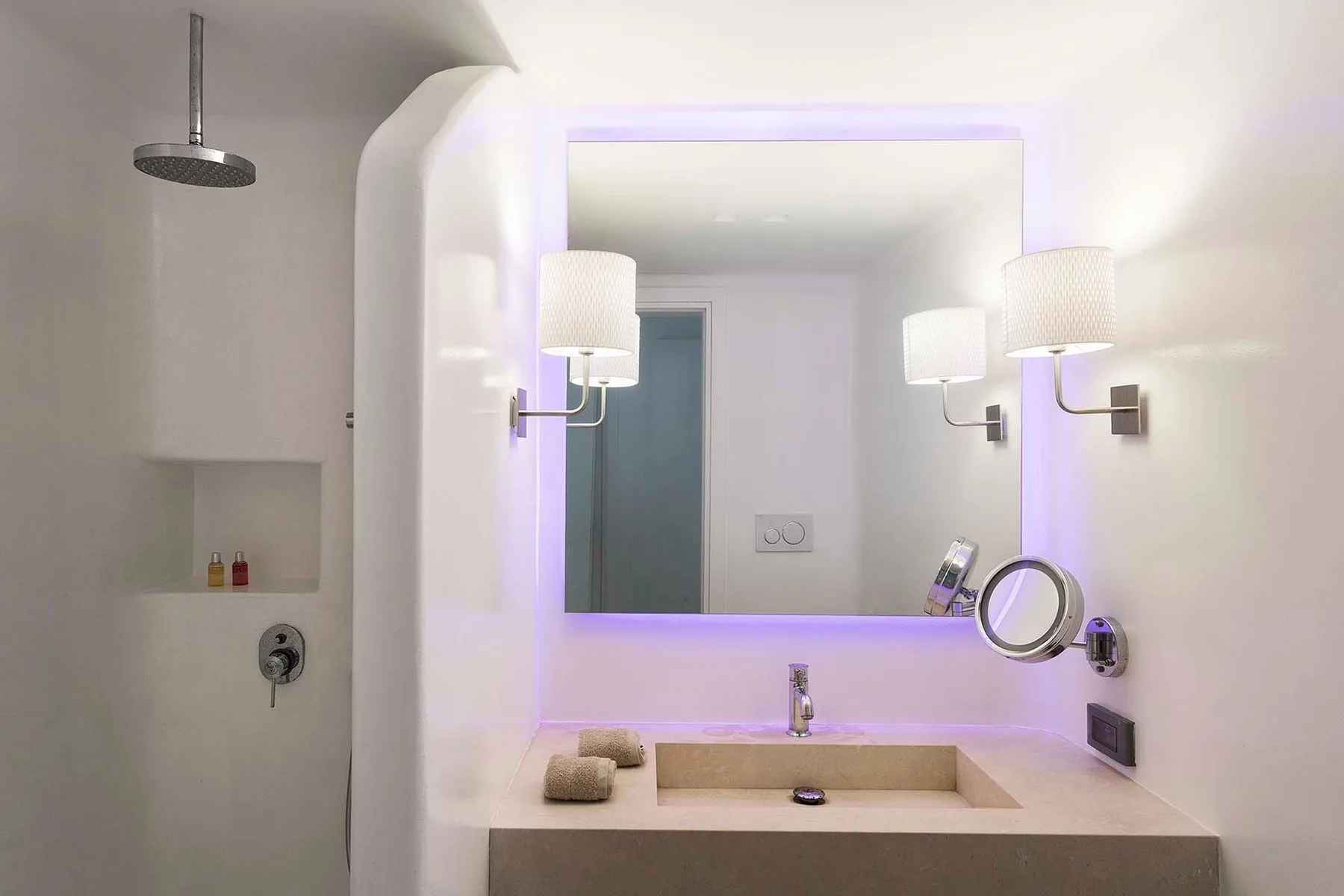 A modern bathroom vanity with a large illuminated mirror and shower.