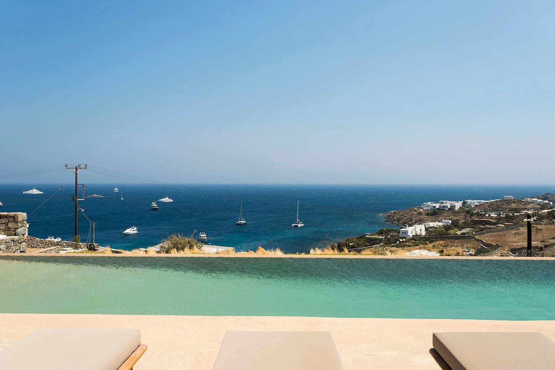 A seaside pool overlooks the blue ocean and boats on the horizon.