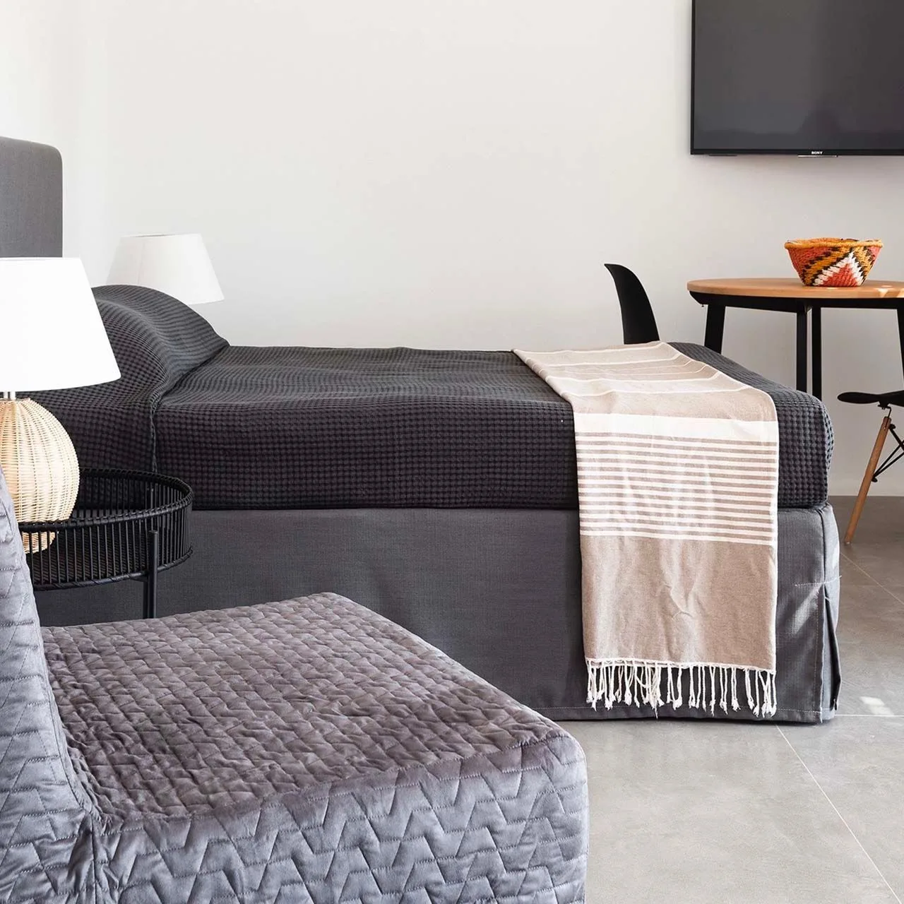 A bedroom with a bed, a draped blanket, and a television on the wall.