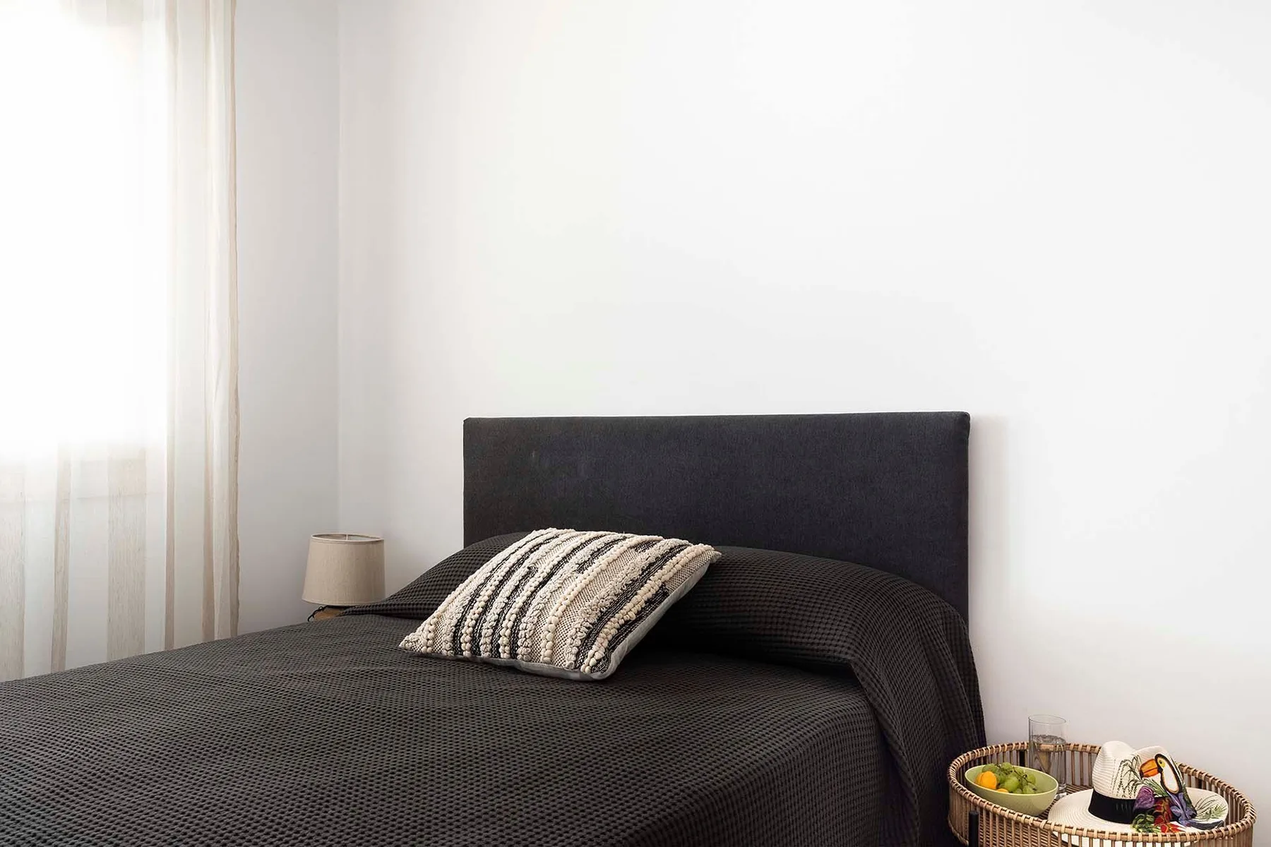 A bedroom with a dark bedspread and a striped pillow beside a bright window.