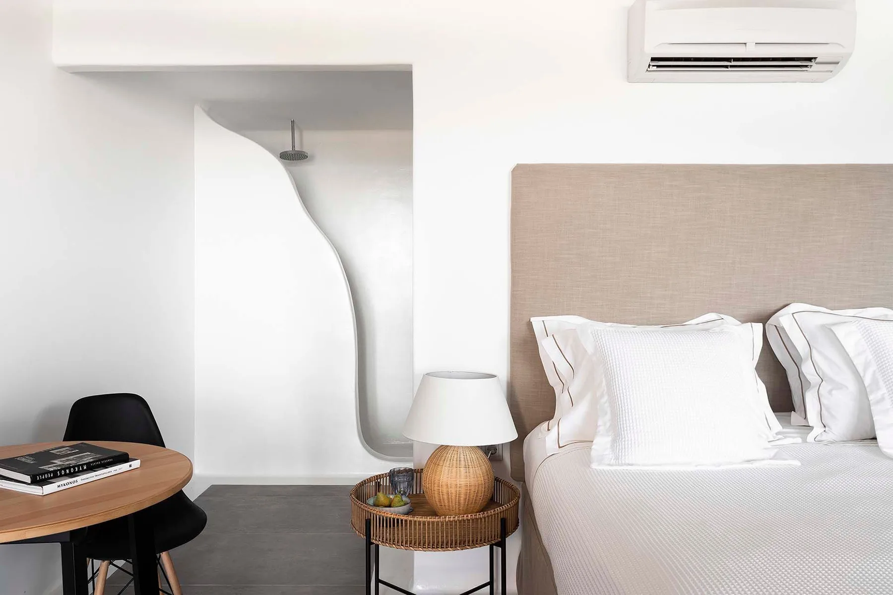 A bedroom with a bed beside a small round table and an open shower area.