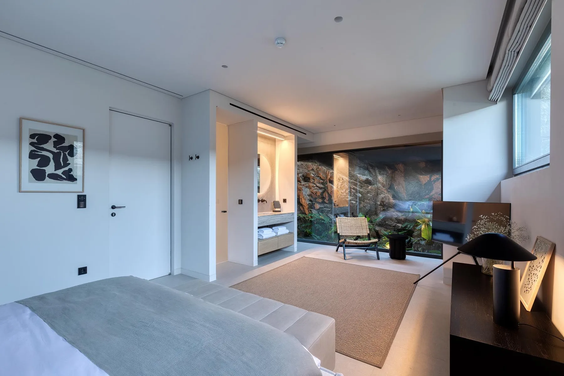 Un dormitorio moderno se abre a una zona de estar, con una gran ventana y vistas al jardín.