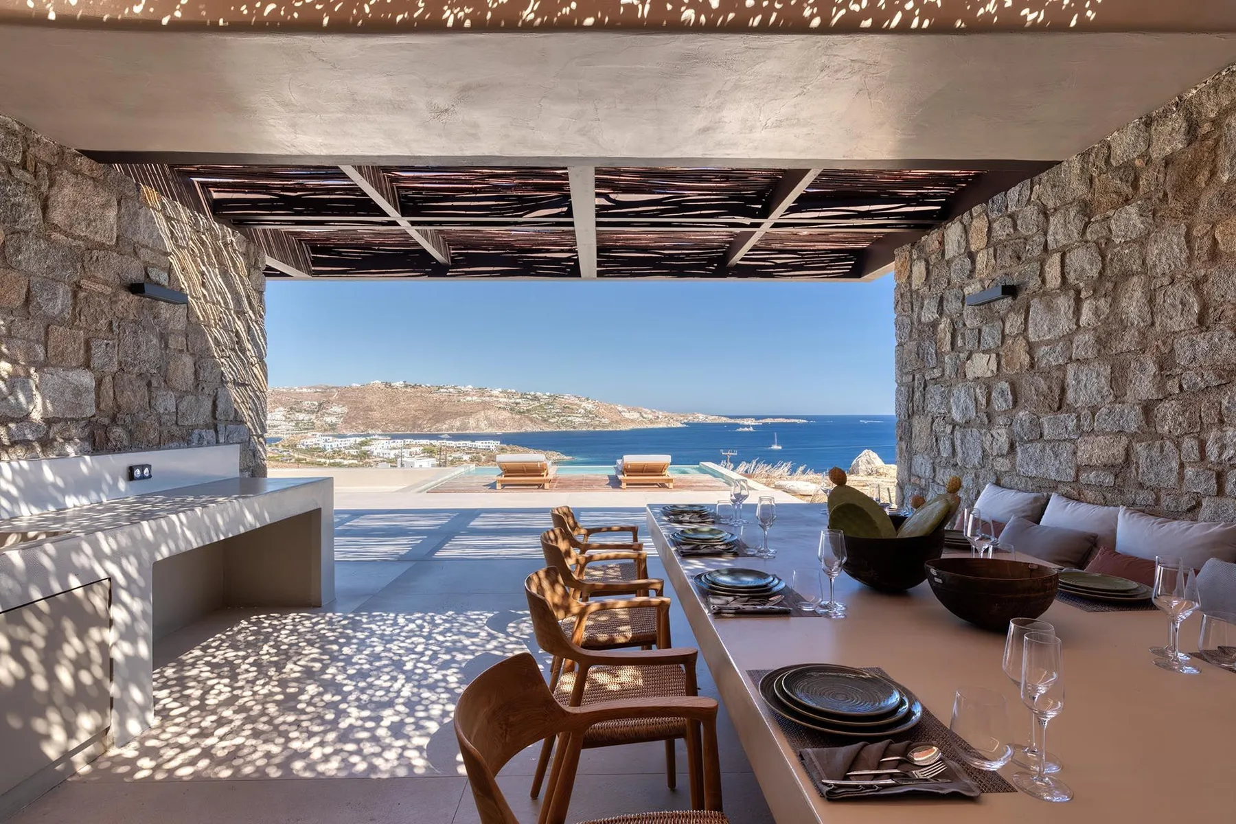 Un comedor exterior cubierto se abre a una vista del mar, con una mesa larga y asientos.
