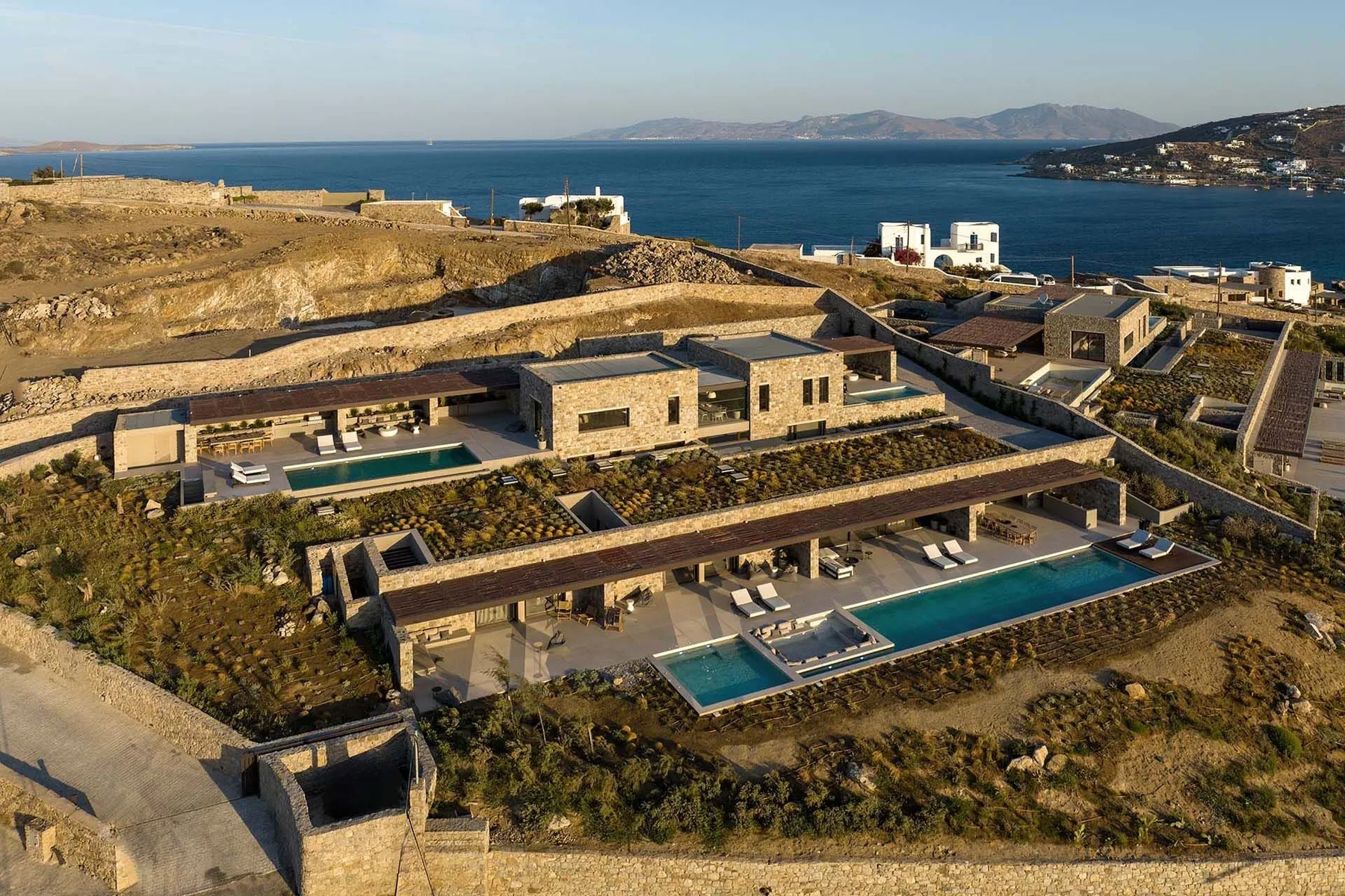 Vista aérea de villas modernas junto al mar con piscinas frente al mar azul.