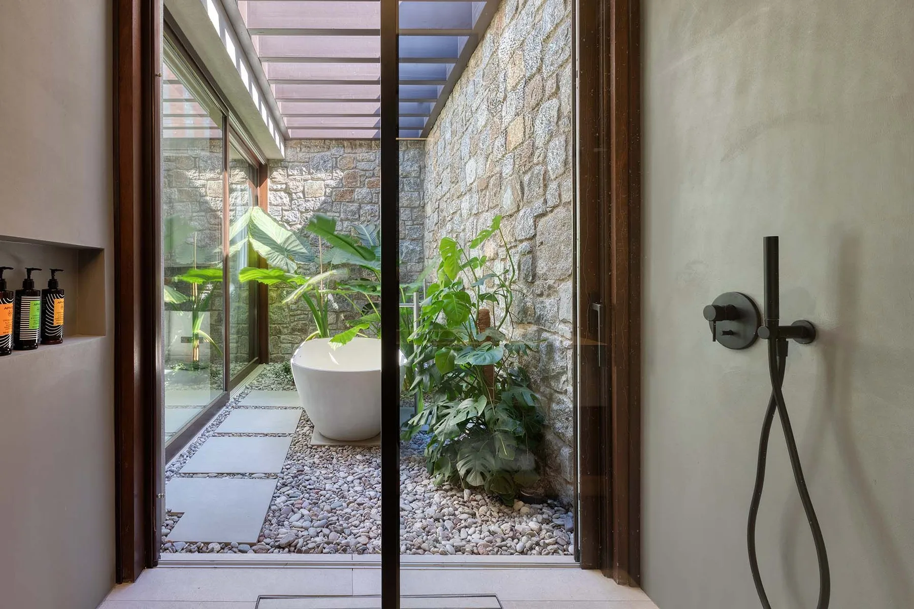Un baño da a un patio acristalado con plantas y una bañera independiente.
