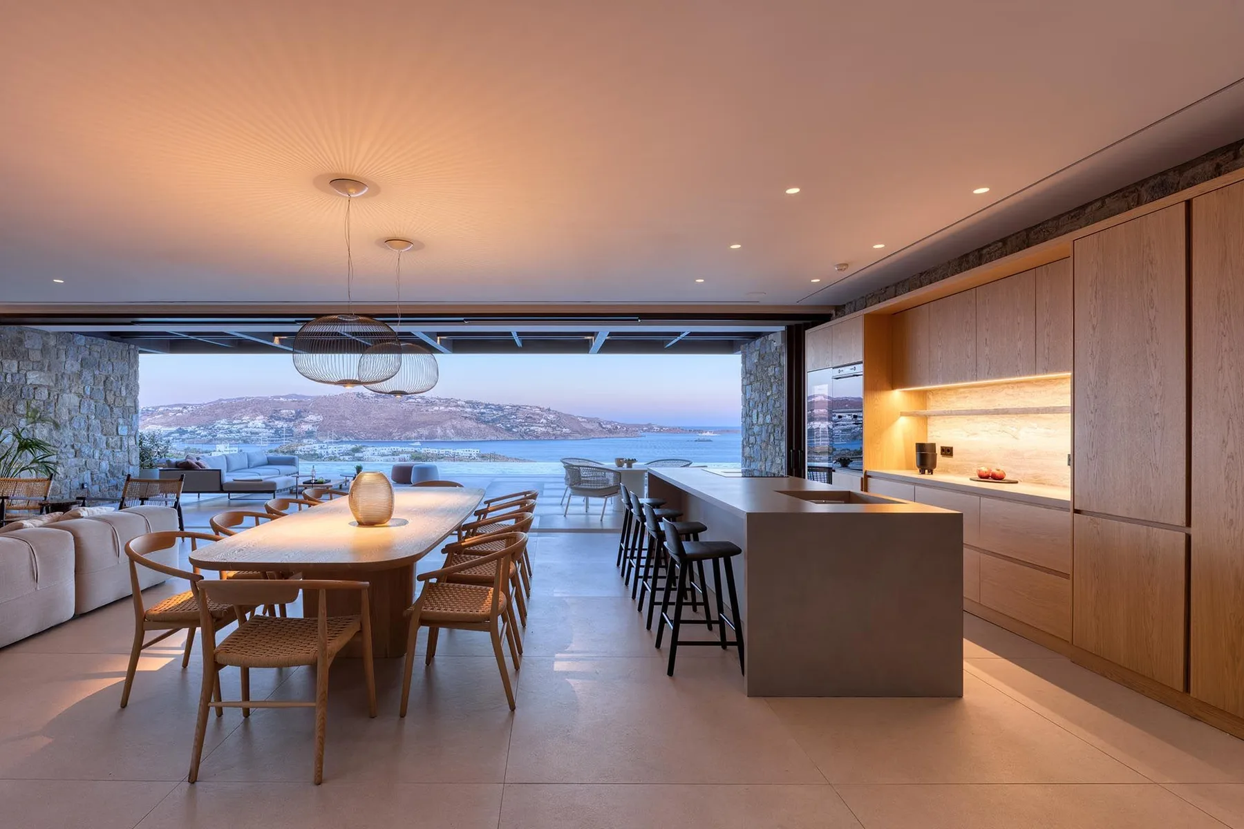 Un comedor de planta abierta y una cocina tienen vistas al agua a través de amplios ventanales.