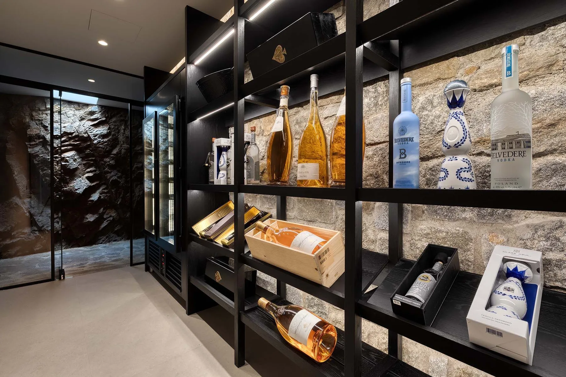 Una exhibición de botellas ocupa estanterías oscuras en una sala con paredes de piedra.