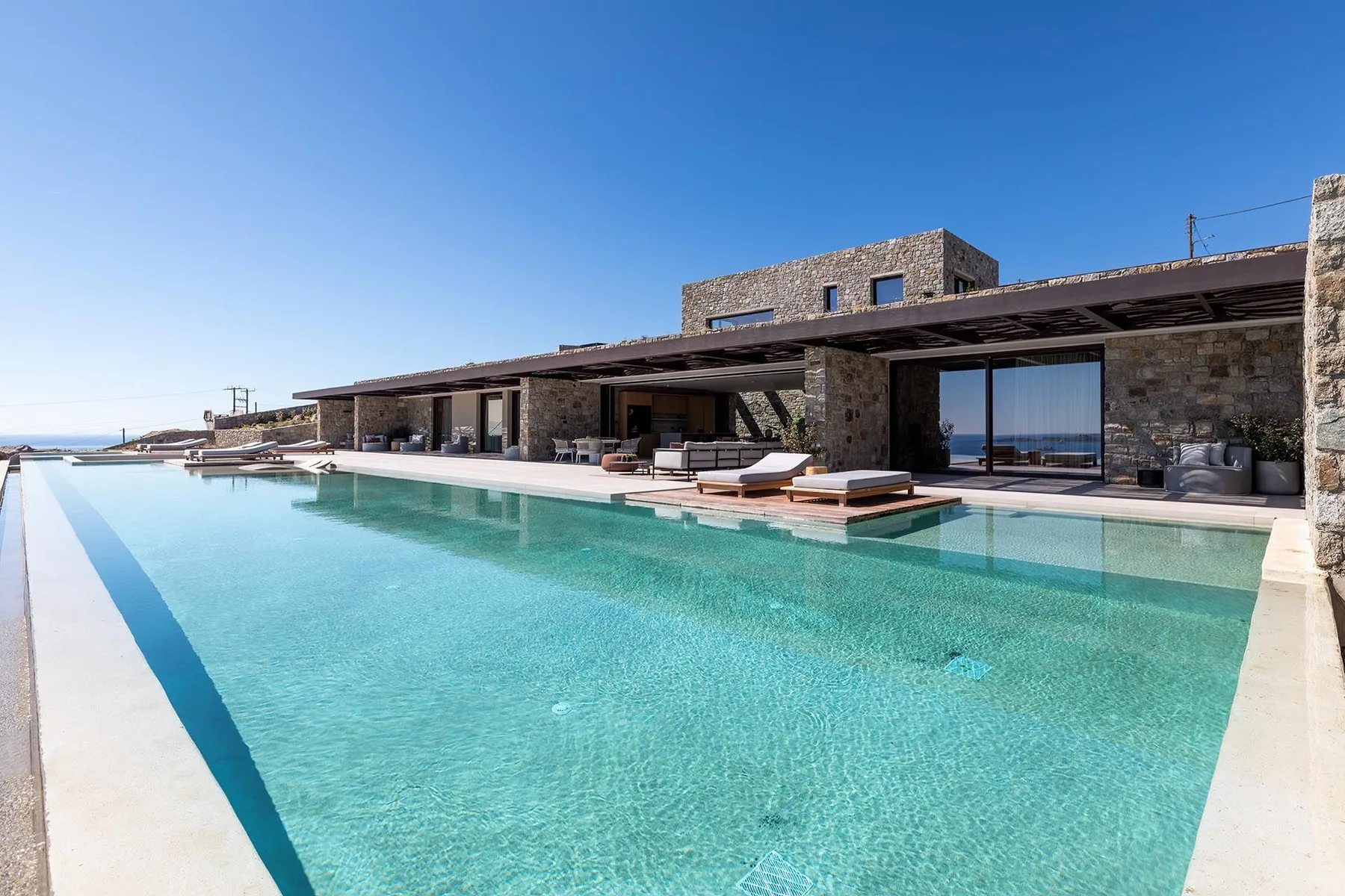 Una larga piscina exterior se extiende junto a un edificio moderno de piedra.