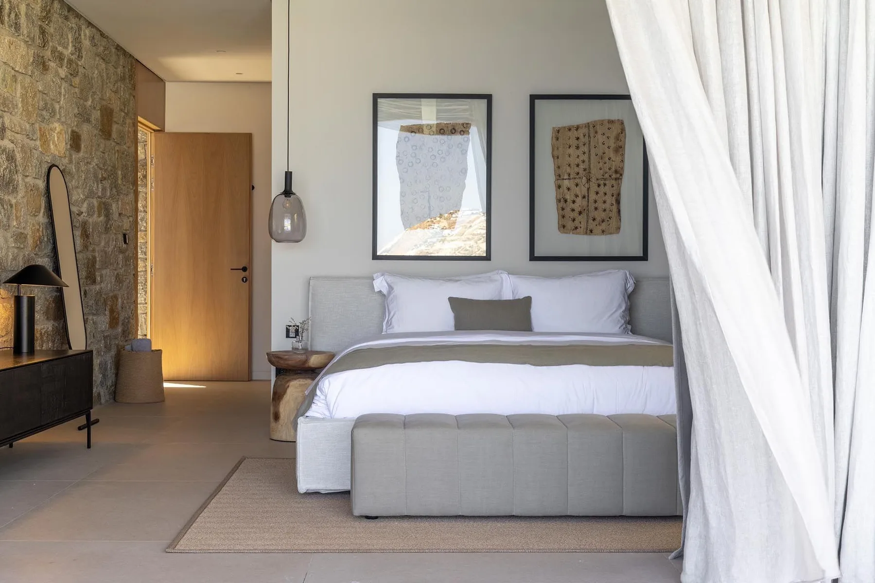 Un dormitorio con una cama tendida, cuadros enmarcados y una pared de piedra.