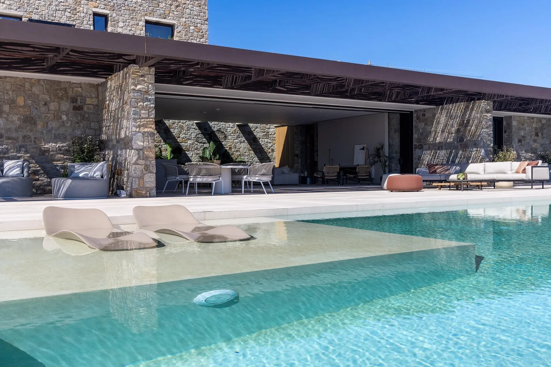 Una piscina con asientos dentro del agua está junto a una sala exterior cubierta.