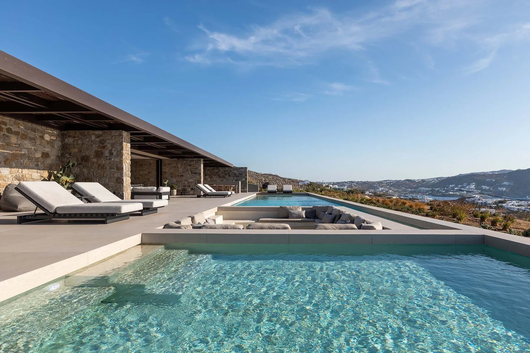 Una piscina al aire libre está junto a una terraza de piedra con asientos.
