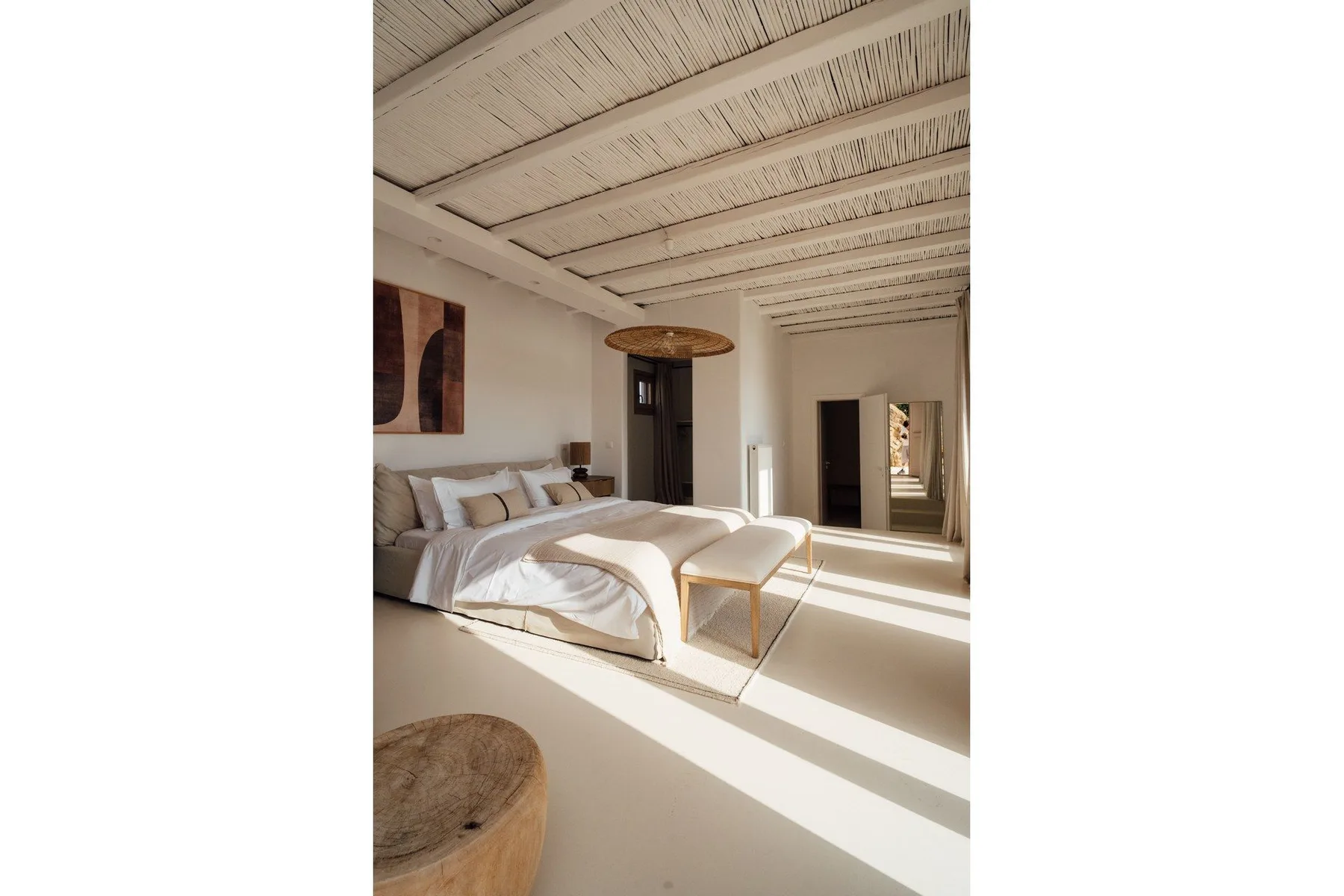 A bright bedroom with a bed beneath a white beamed ceiling.