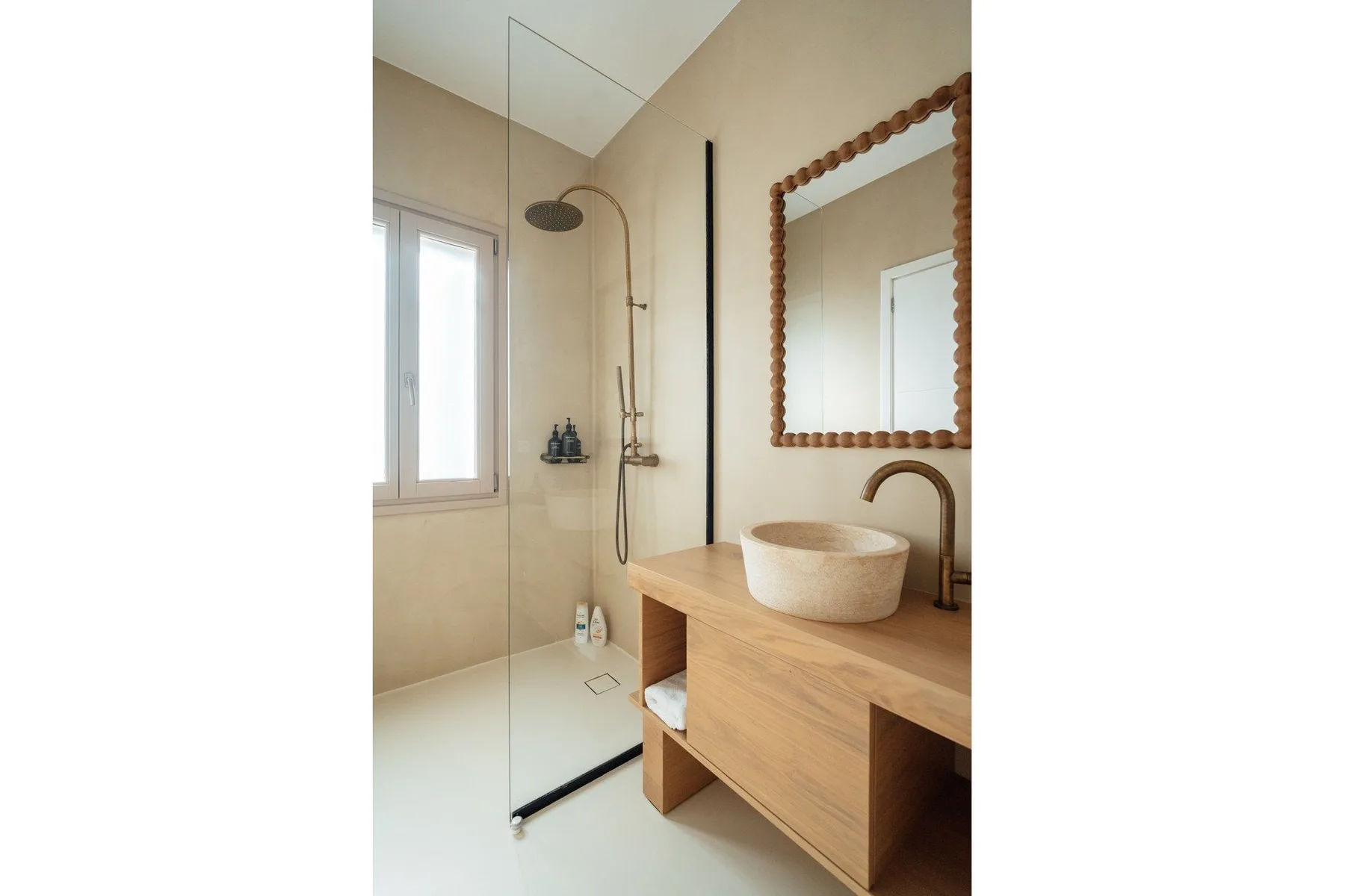 A bright bathroom with a glass shower, wood vanity, and round vessel sink.
