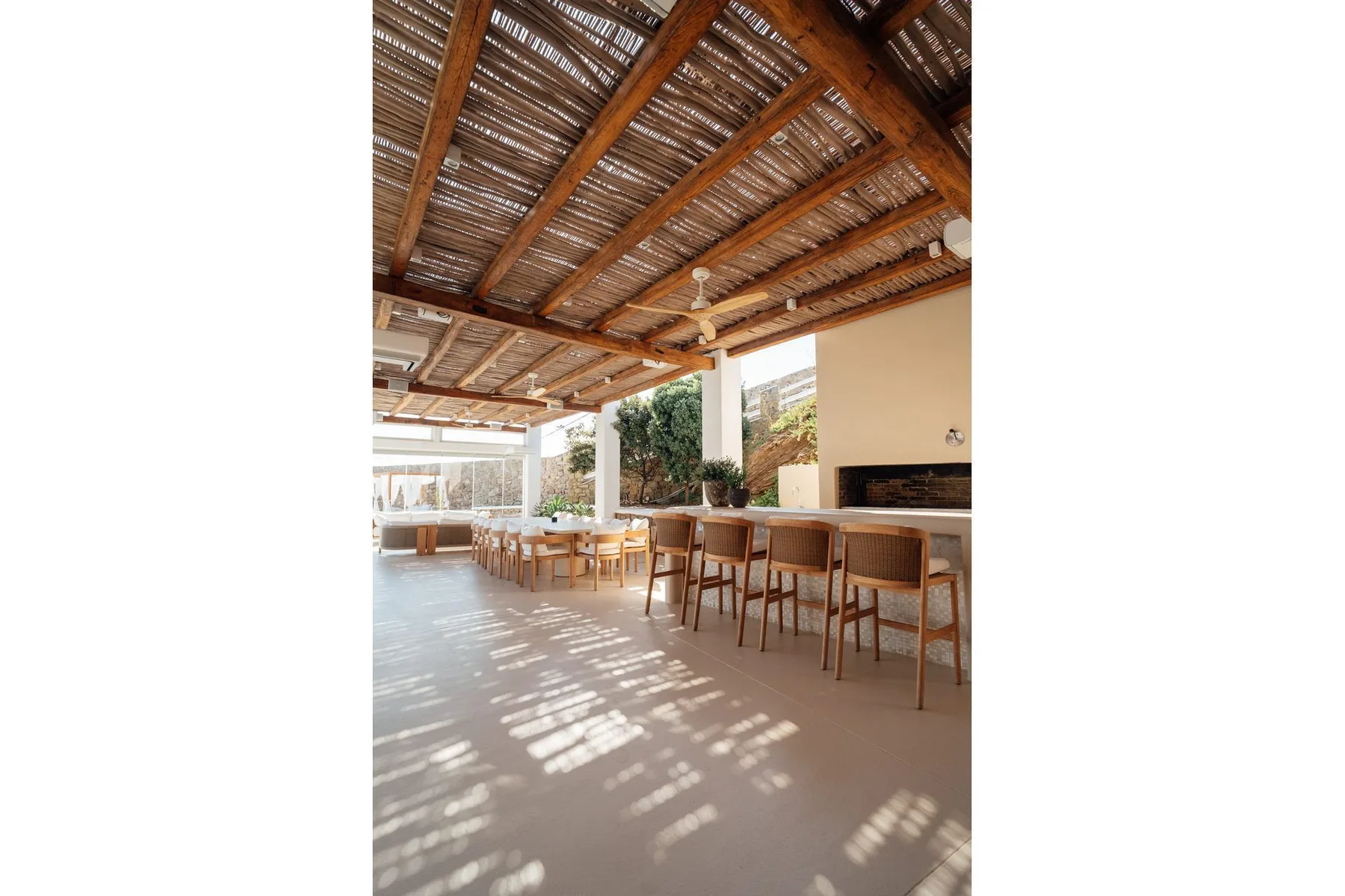 A covered outdoor dining area with a long table and seating beneath a timber roof.