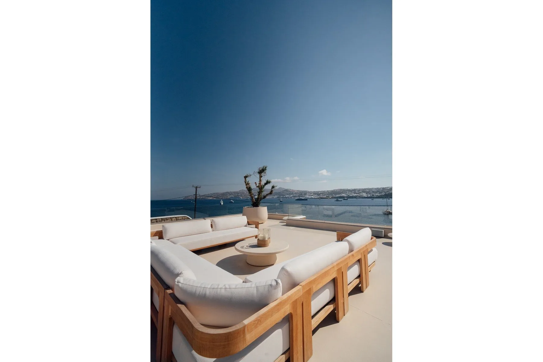 An outdoor waterfront seating area with cushioned wooden benches and a small table.