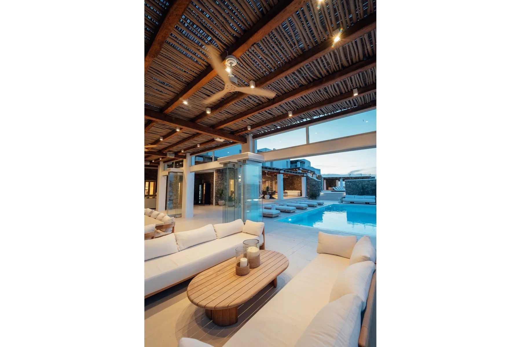 An open living area with seating and a pool visible beyond the glass doors.