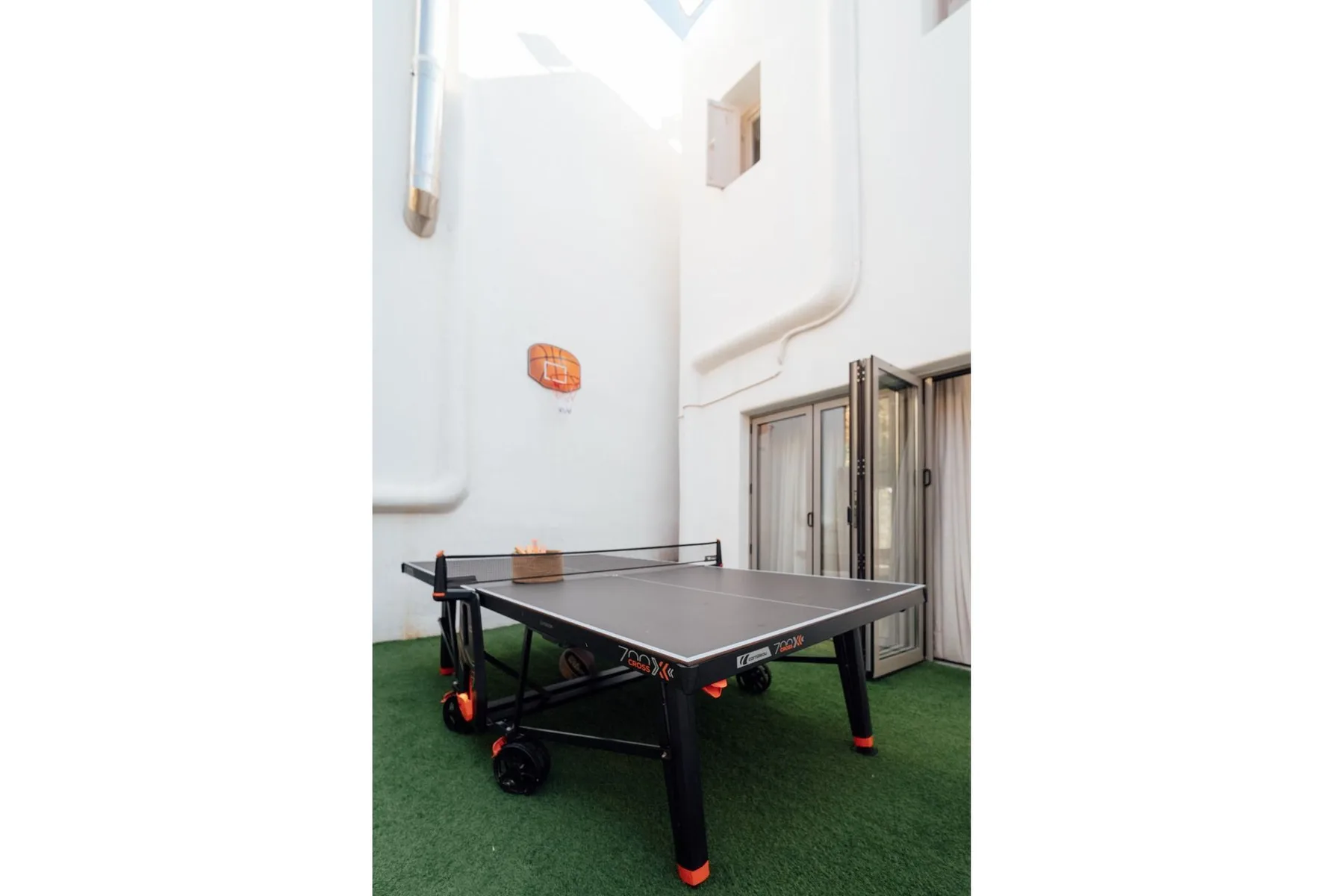 A ping-pong table sits on green flooring beside tall windows.