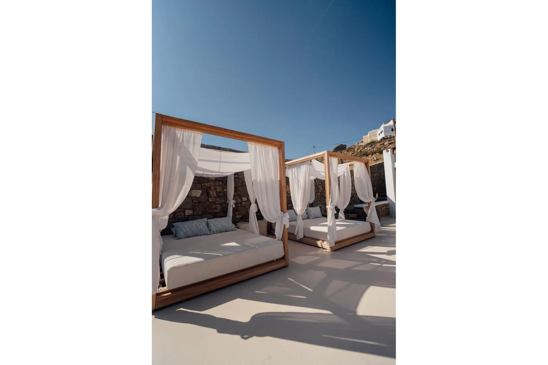 An outdoor terrace with curtained daybeds under a clear blue sky.