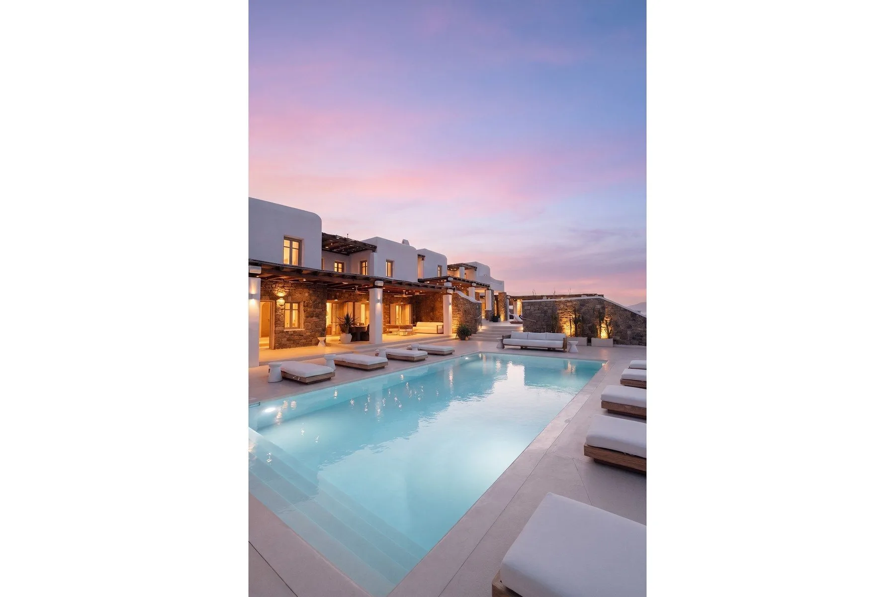 An outdoor swimming pool sits beside illuminated buildings at dusk.