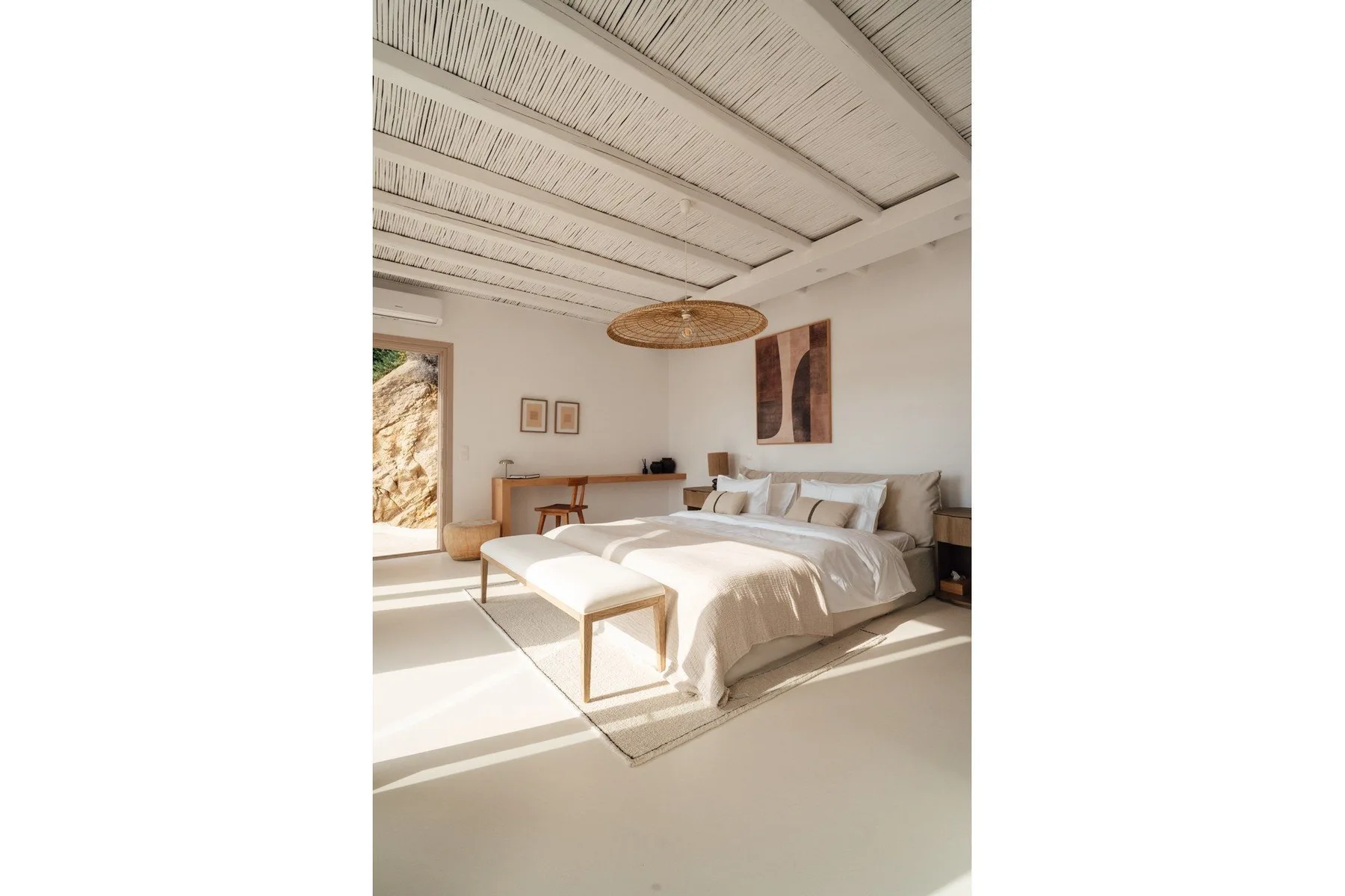 A bright bedroom with a bed, a small table, and sunlight across the floor.