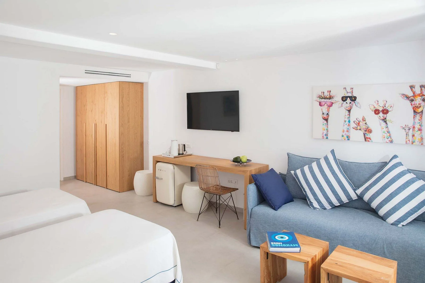 A bright bedroom with a blue sofa, bed, and wooden desk beneath a wall-mounted television.