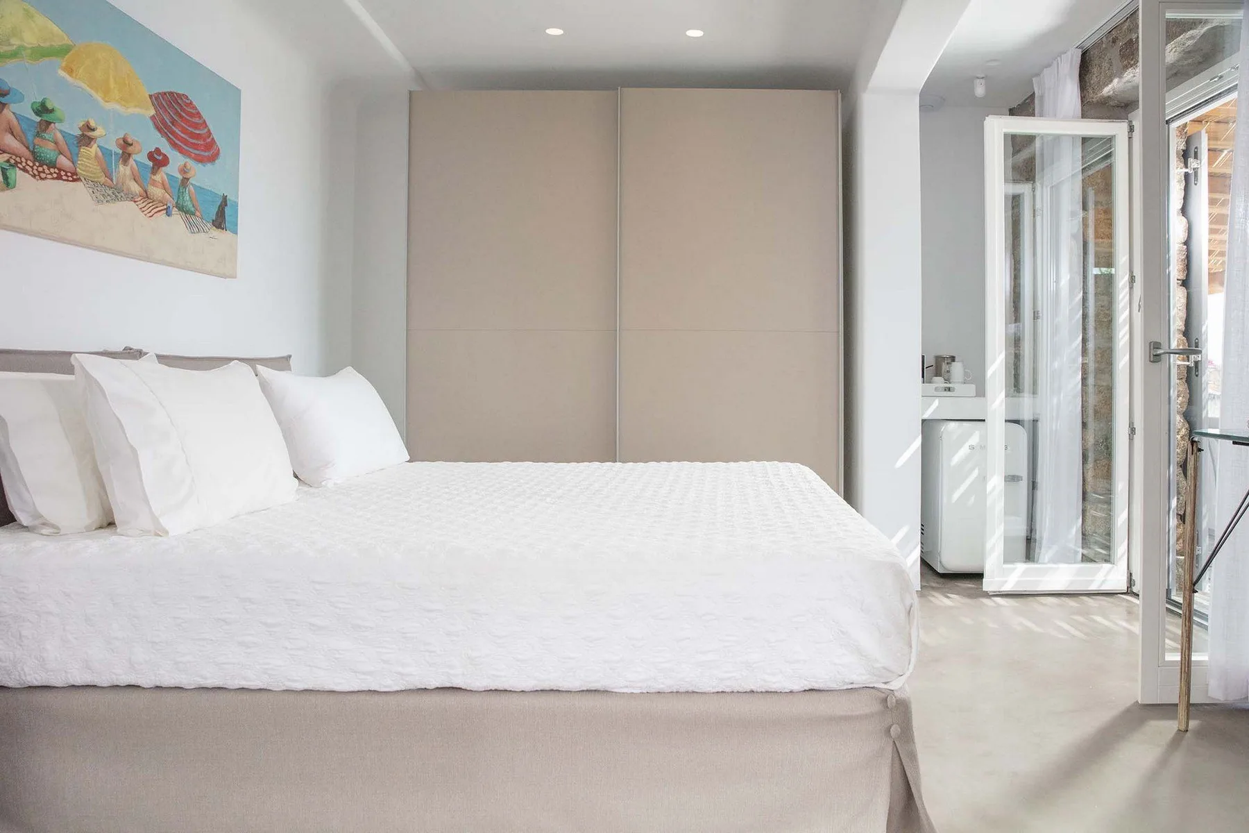 A bright bedroom with a neatly made bed and an open glass door.