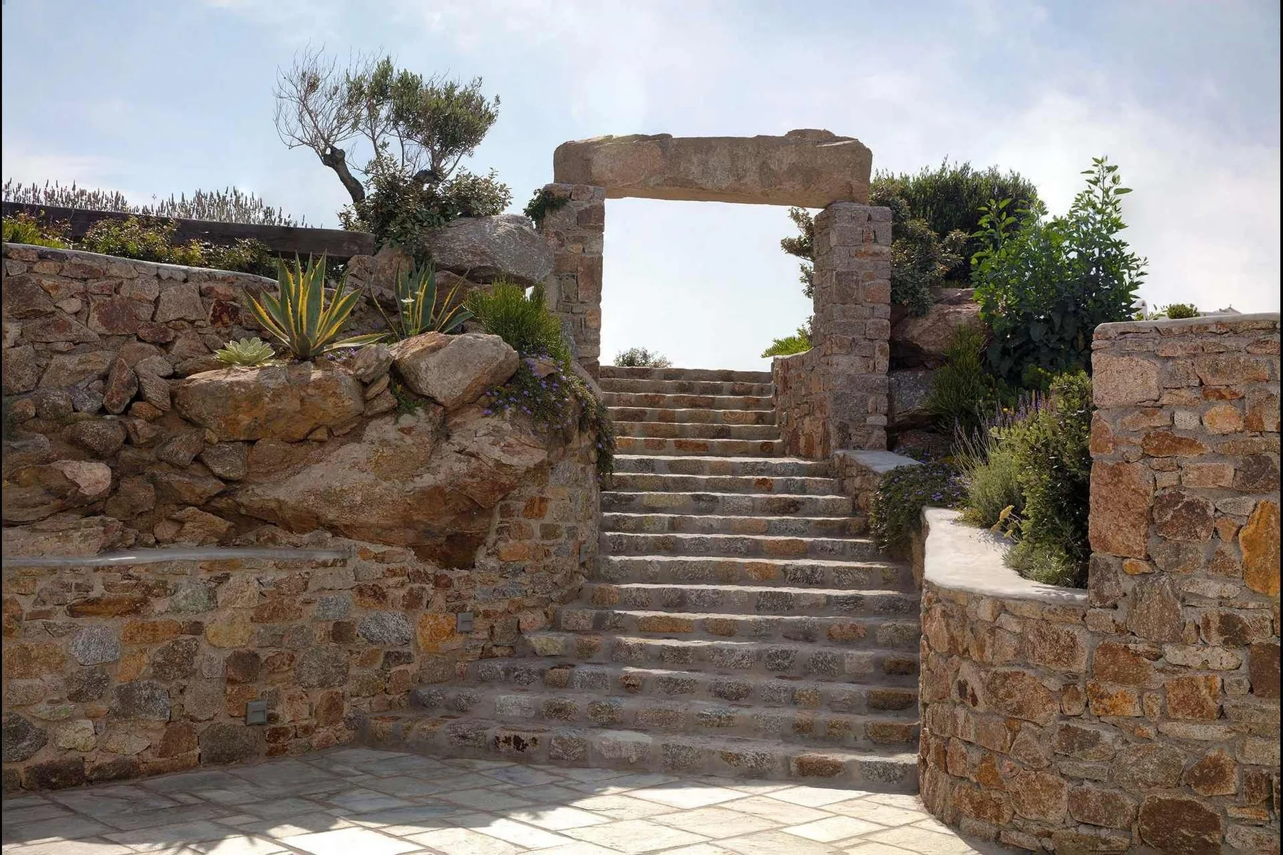 Stone steps lead through a garden entrance framed by low stone walls.