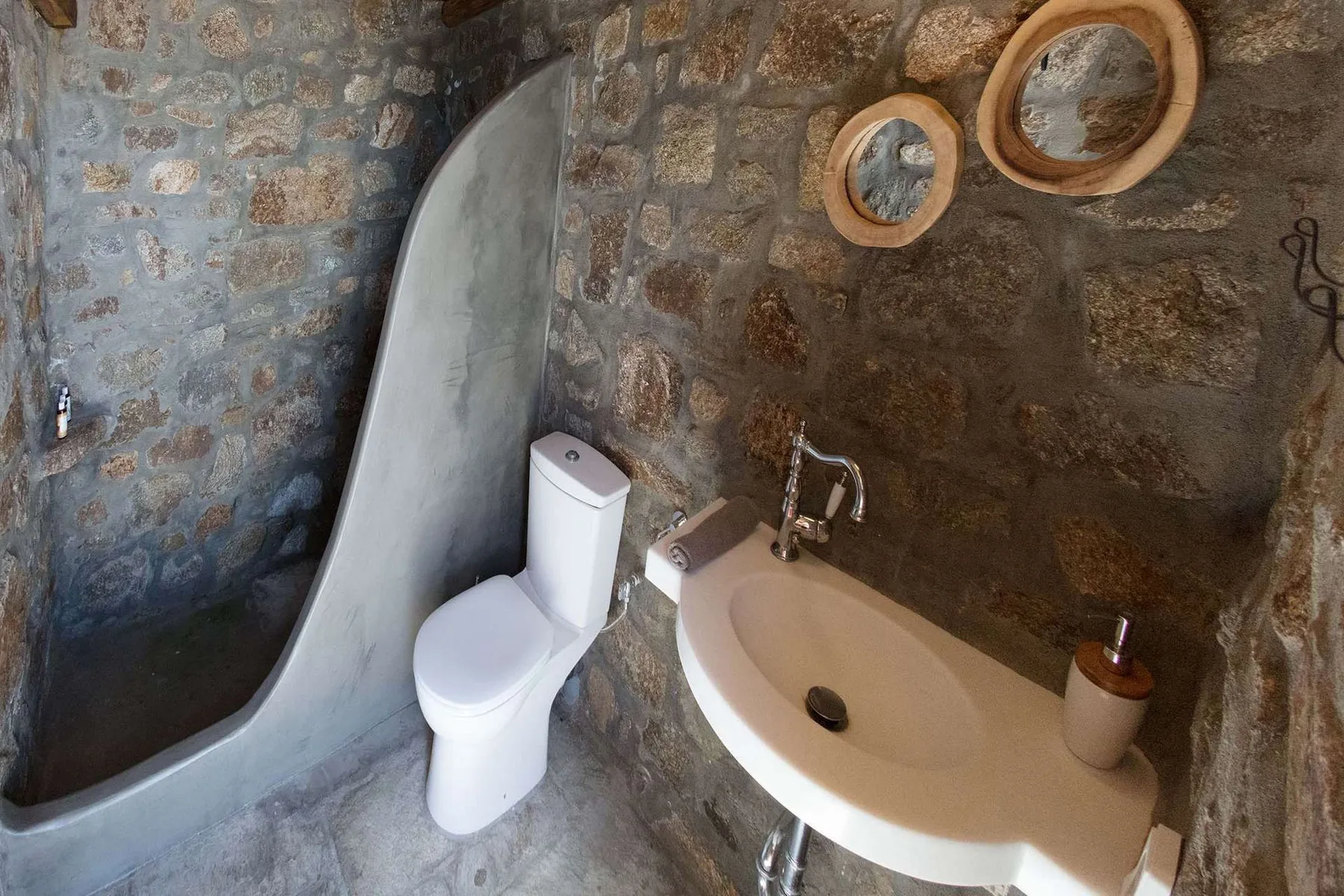 A bathroom with a toilet and a wall-mounted sink against stone walls.