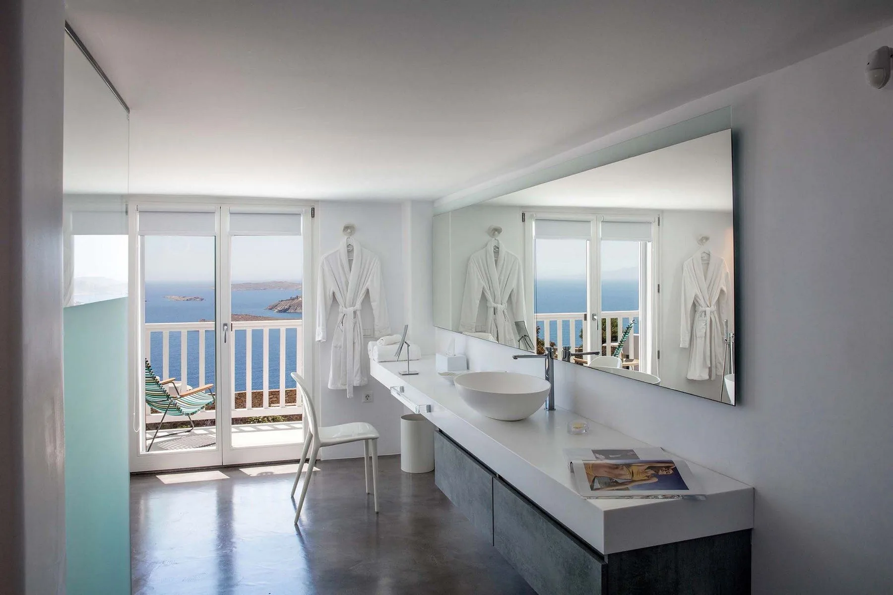 A bright bathroom with a long vanity and a sea view through glass doors.