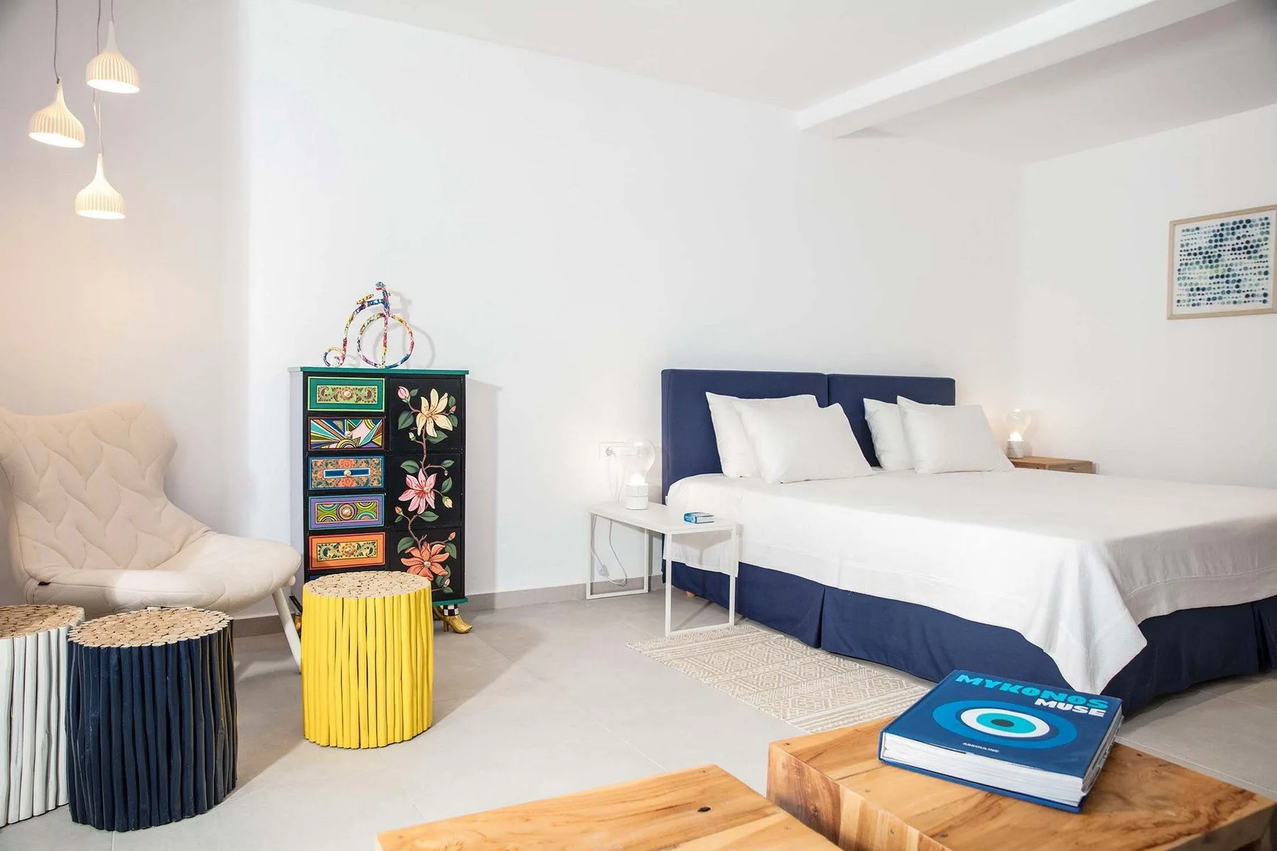 A bright bedroom with a large bed, colorful drawers, and a small seating area.