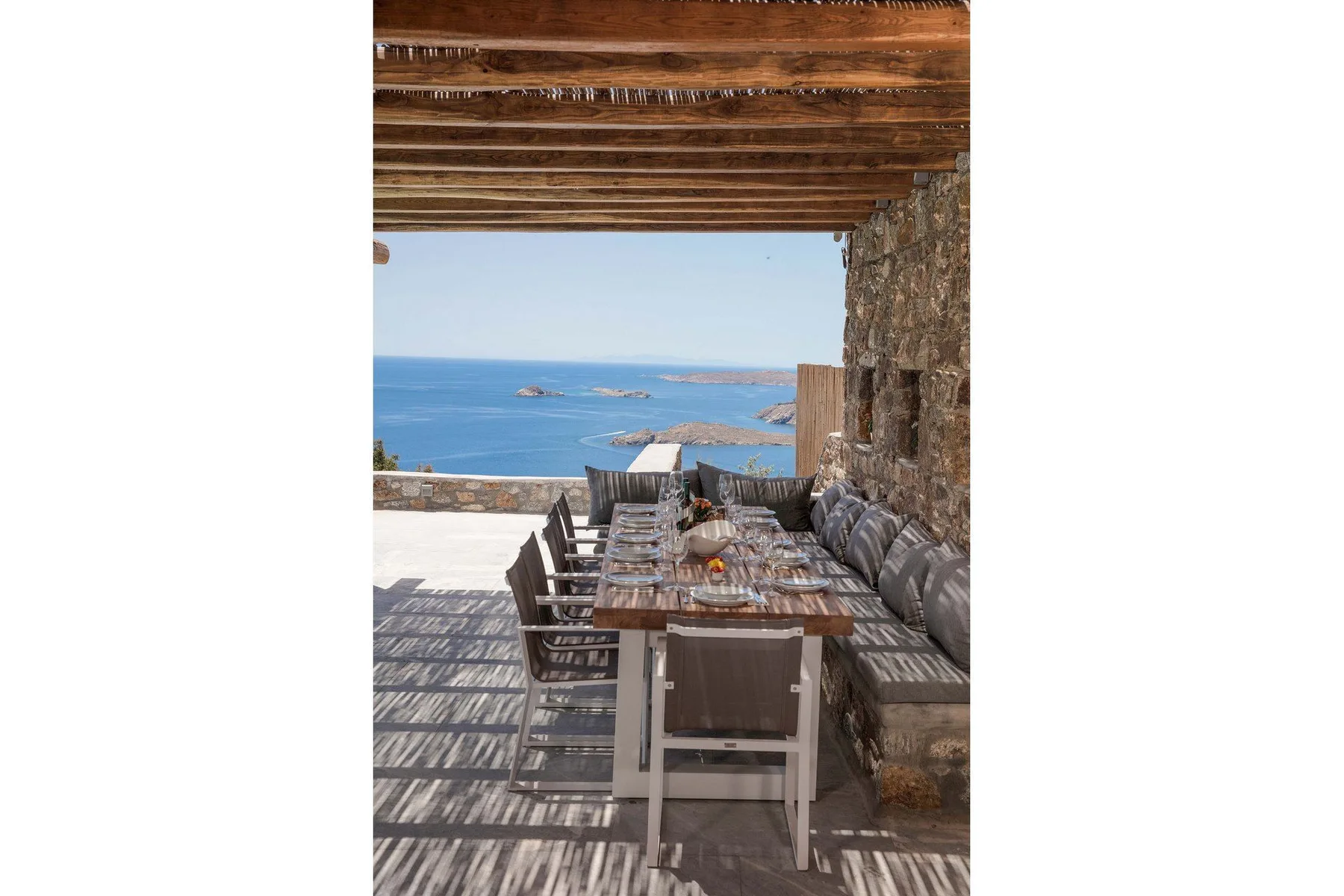 An outdoor dining area beneath a wooden pergola overlooks the sea.