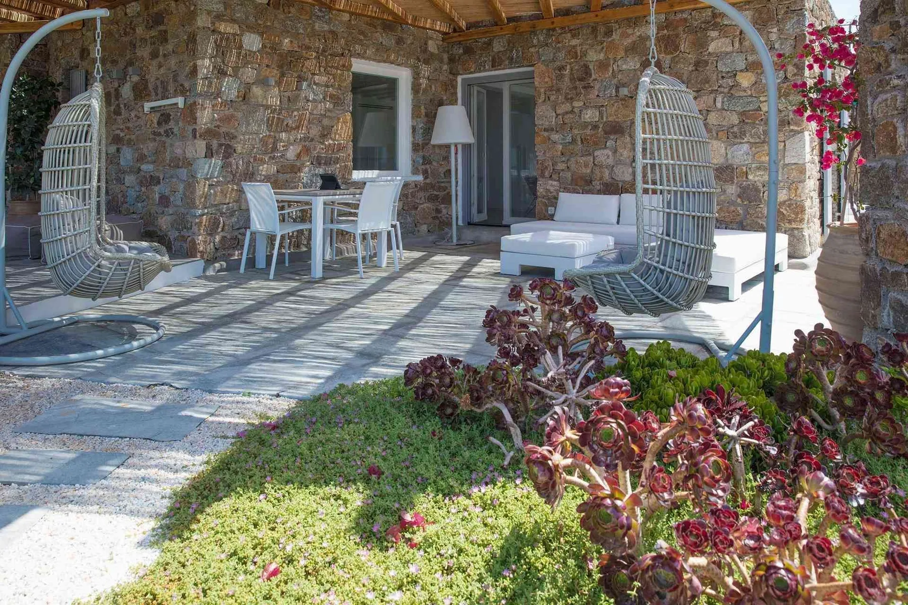 A covered stone patio with a dining table, hanging chairs, and outdoor seating.