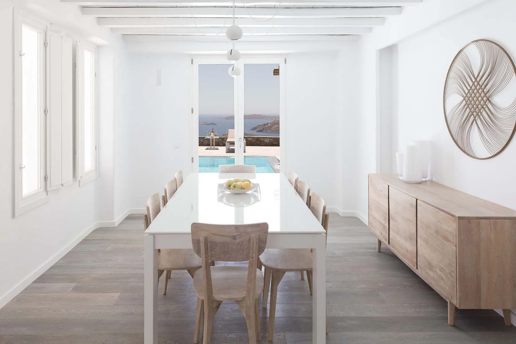 A bright dining area features a long table and chairs beside large windows.