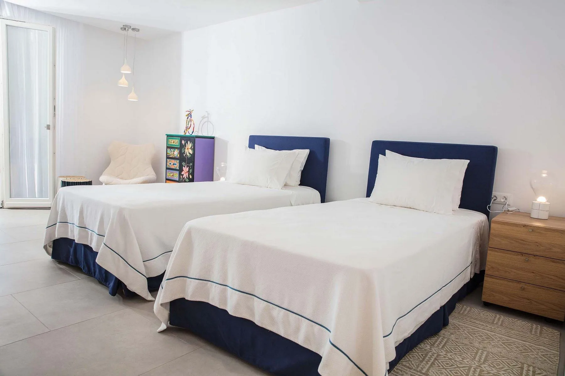 A bedroom with two beds, white bedding, and a wooden bedside table.