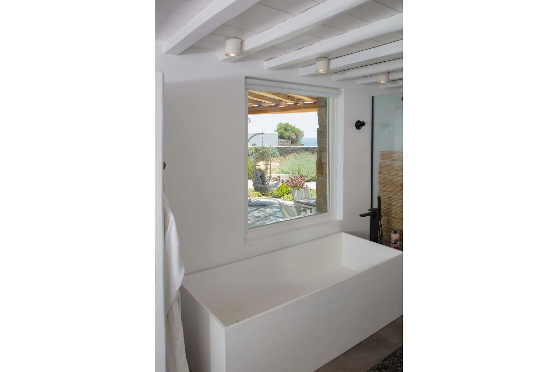 A bright bathroom with a large white bathtub beneath a window overlooking a garden.