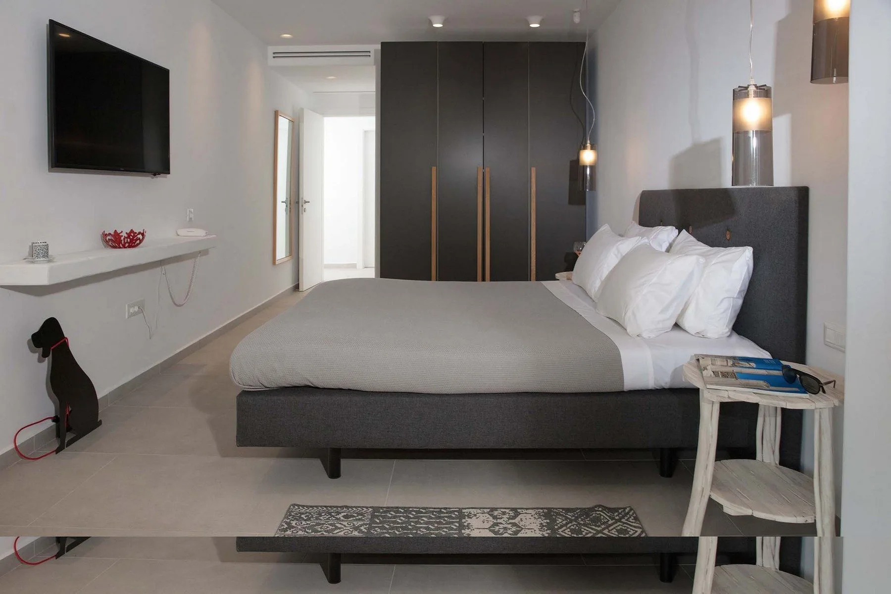 A bedroom with a large bed, dark headboard, and wall-mounted television.