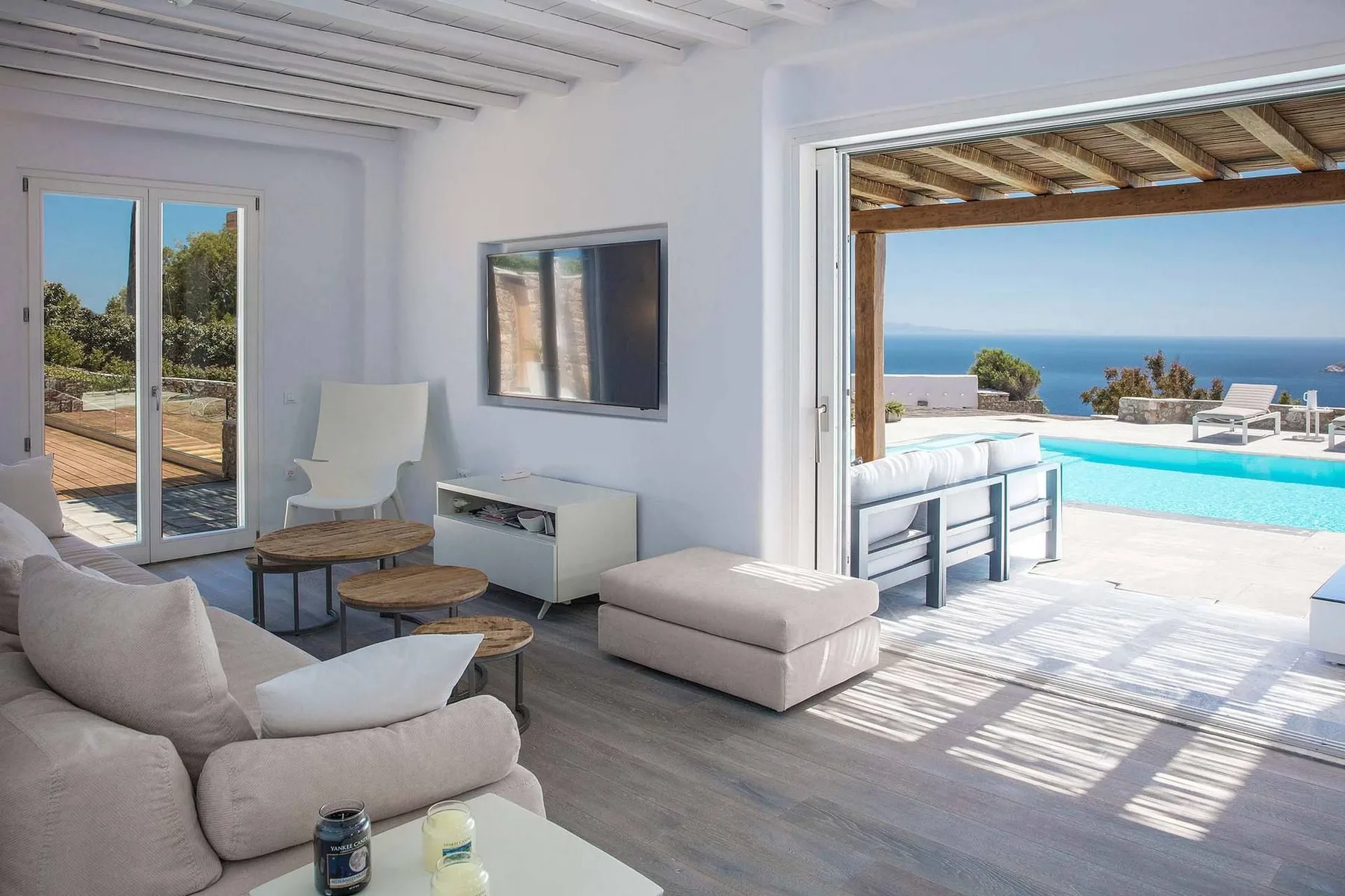 A bright living room opens onto a patio with a swimming pool and ocean view.