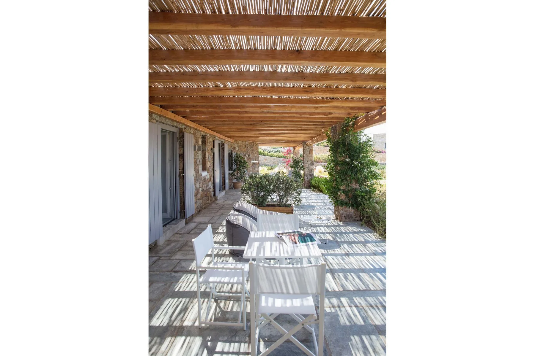 A shaded outdoor dining area sits beneath a wooden pergola beside the building.