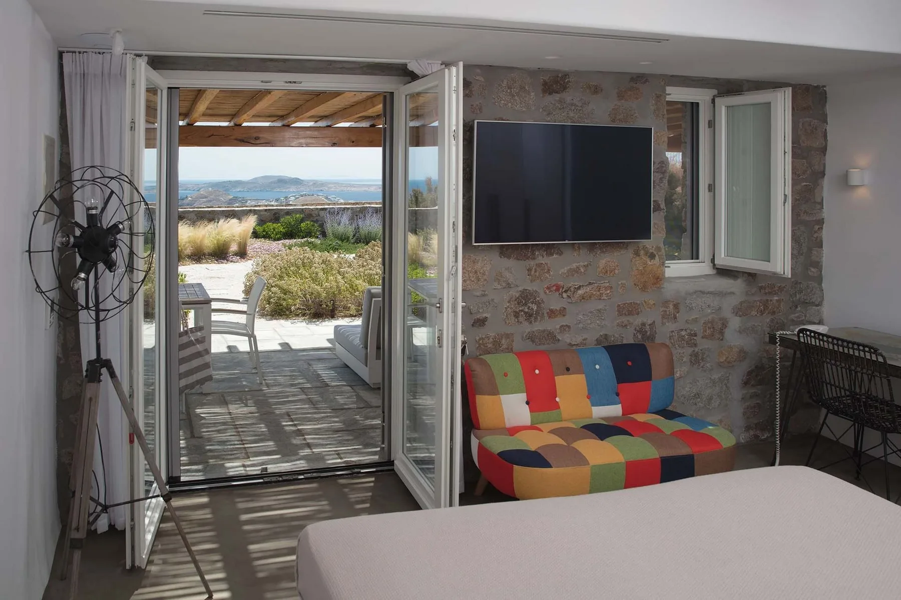 A room with a colorful sofa and an open glass door leading to a patio.