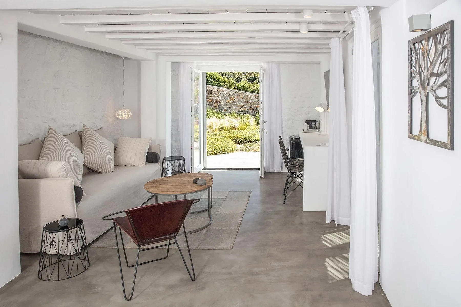 A bright living room with seating and a coffee table beside an open doorway to greenery.