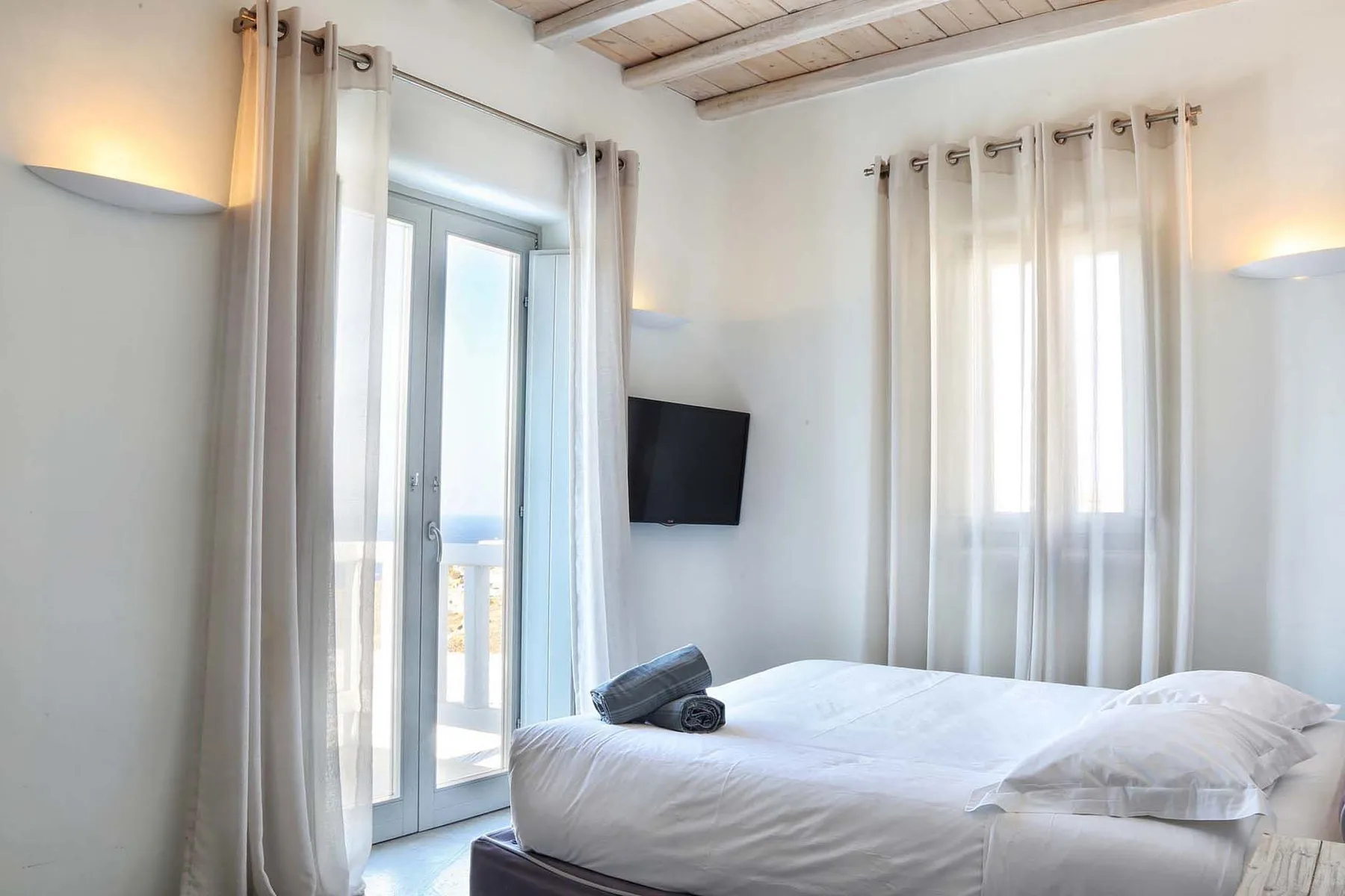 A bright bedroom with a bed beside tall curtained windows.