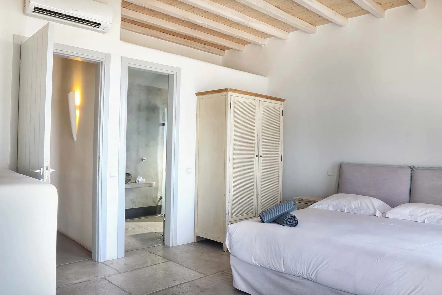 A bright bedroom with a bed, wardrobe, and open doorway to a bathroom.