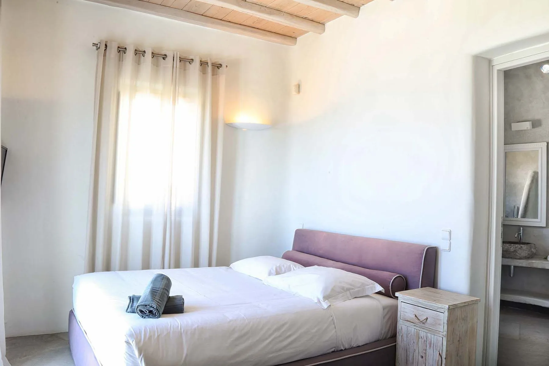 A bright bedroom with a bed beside a curtained window.
