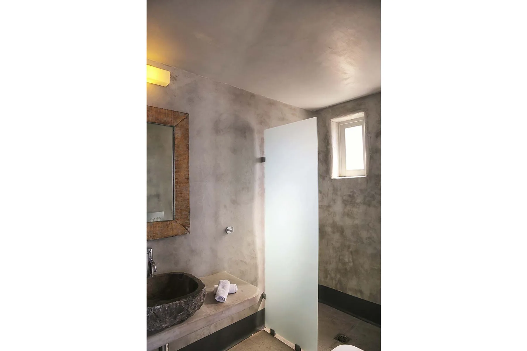 A bathroom with a stone sink, mirror, and frosted glass partition.