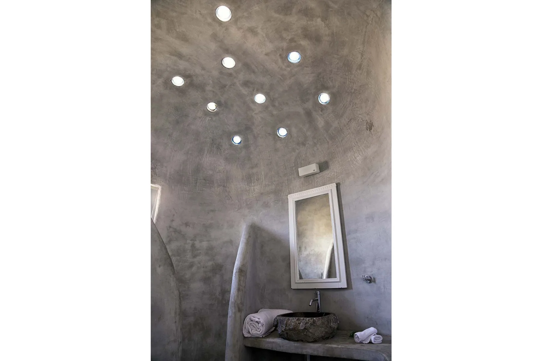 A curved bathroom wall with a mirror, stone sink, and recessed lights.