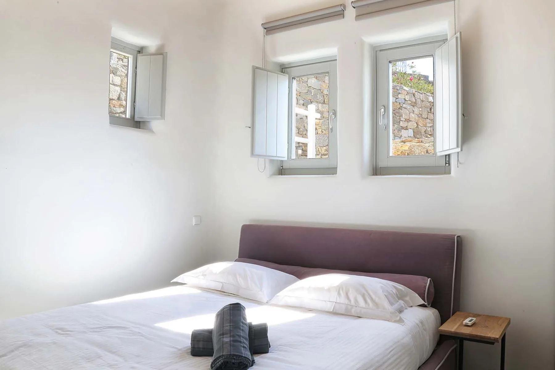 A bedroom with a bed beneath two open windows.