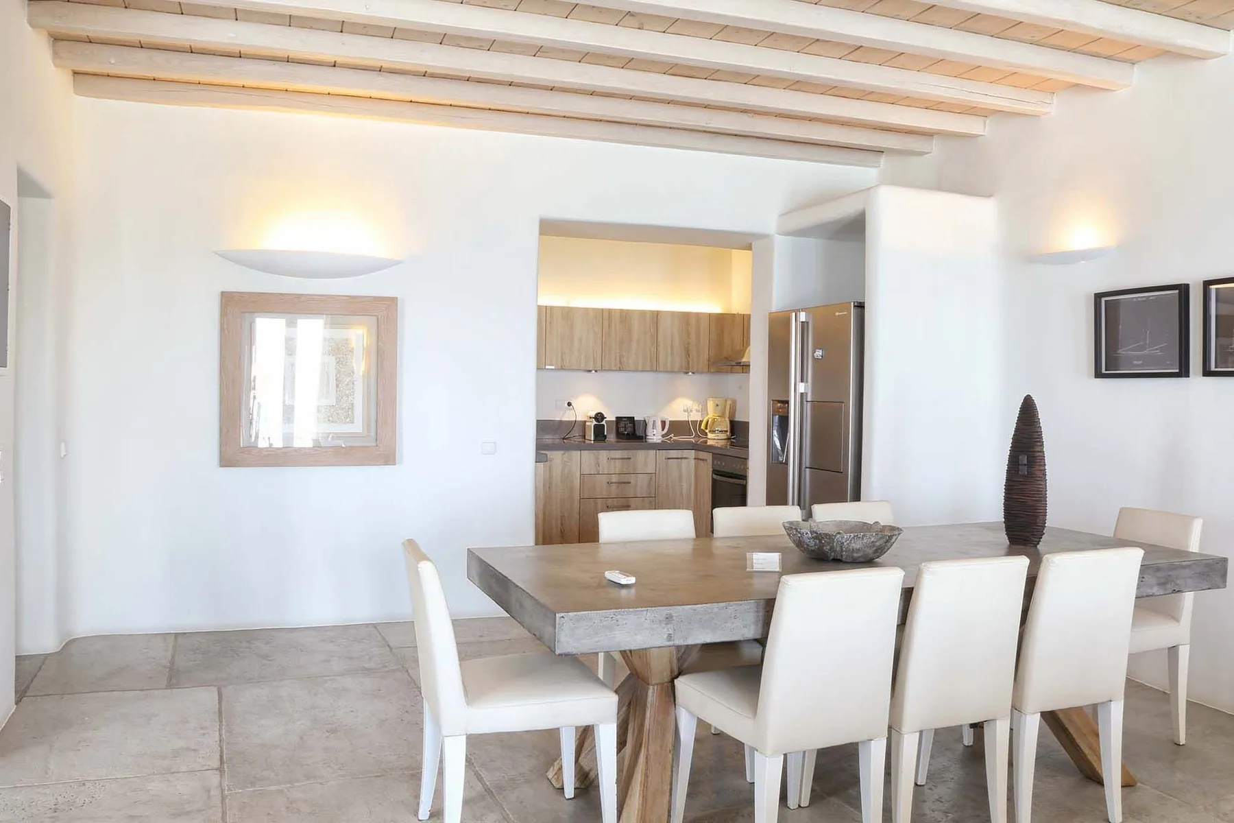 A dining area with a long table and white seating beside an open kitchen.