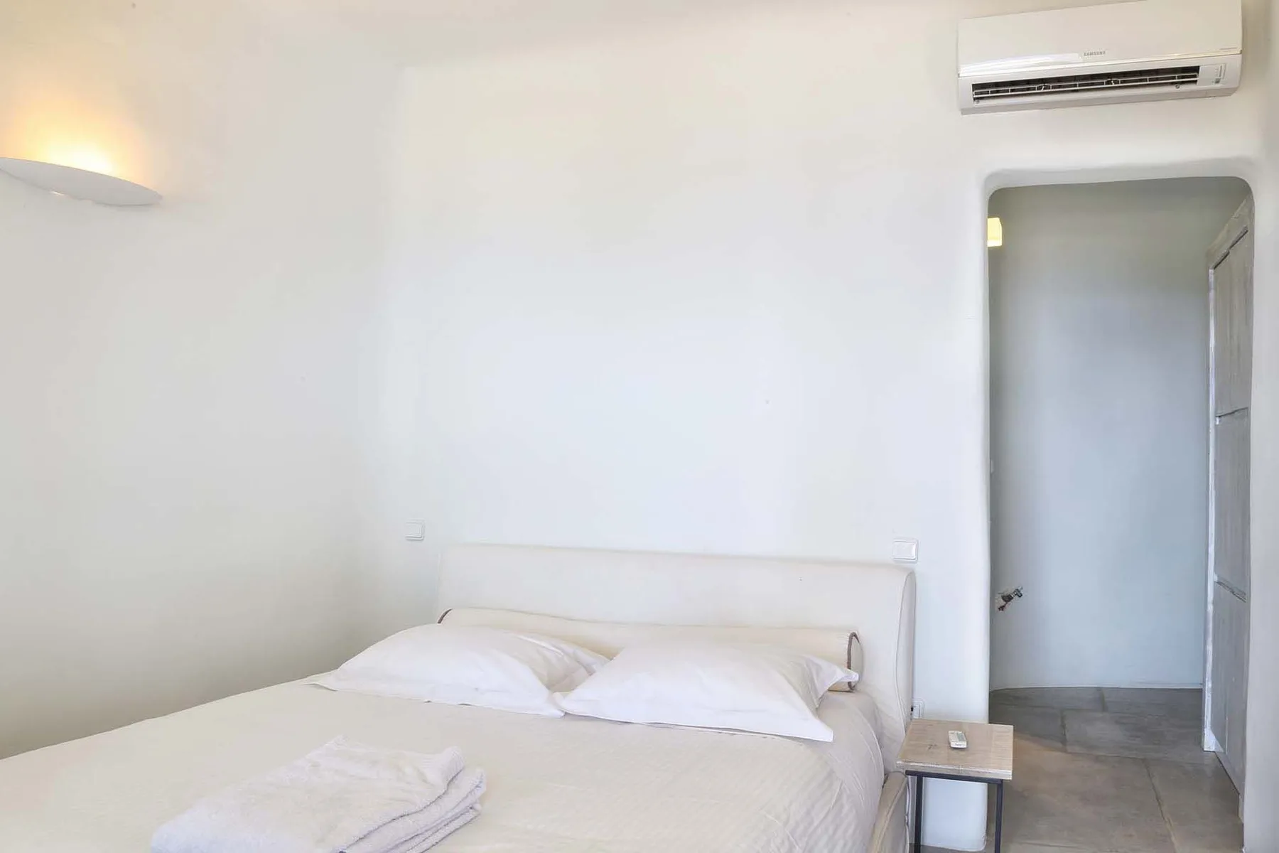 A bright bedroom with a neatly made bed and an open doorway.
