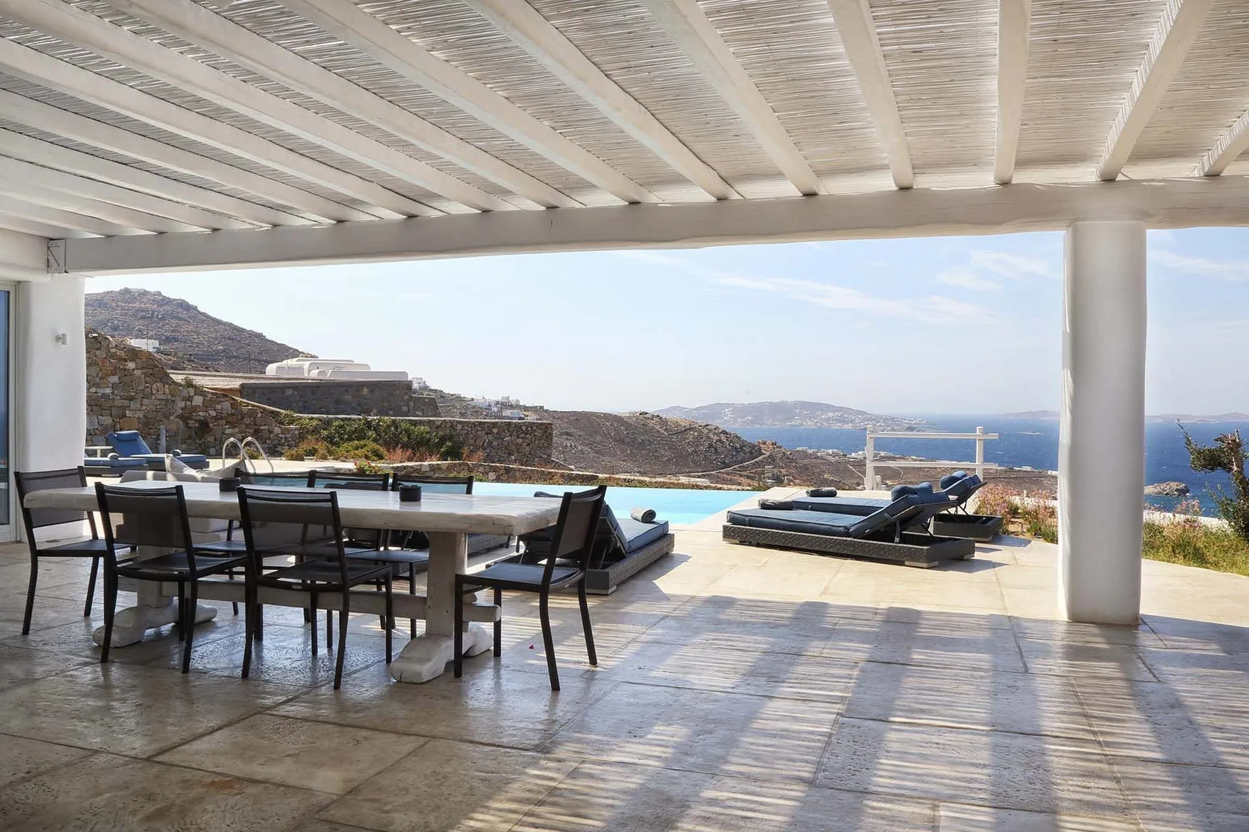 A shaded outdoor dining area opens onto a terrace overlooking the sea.
