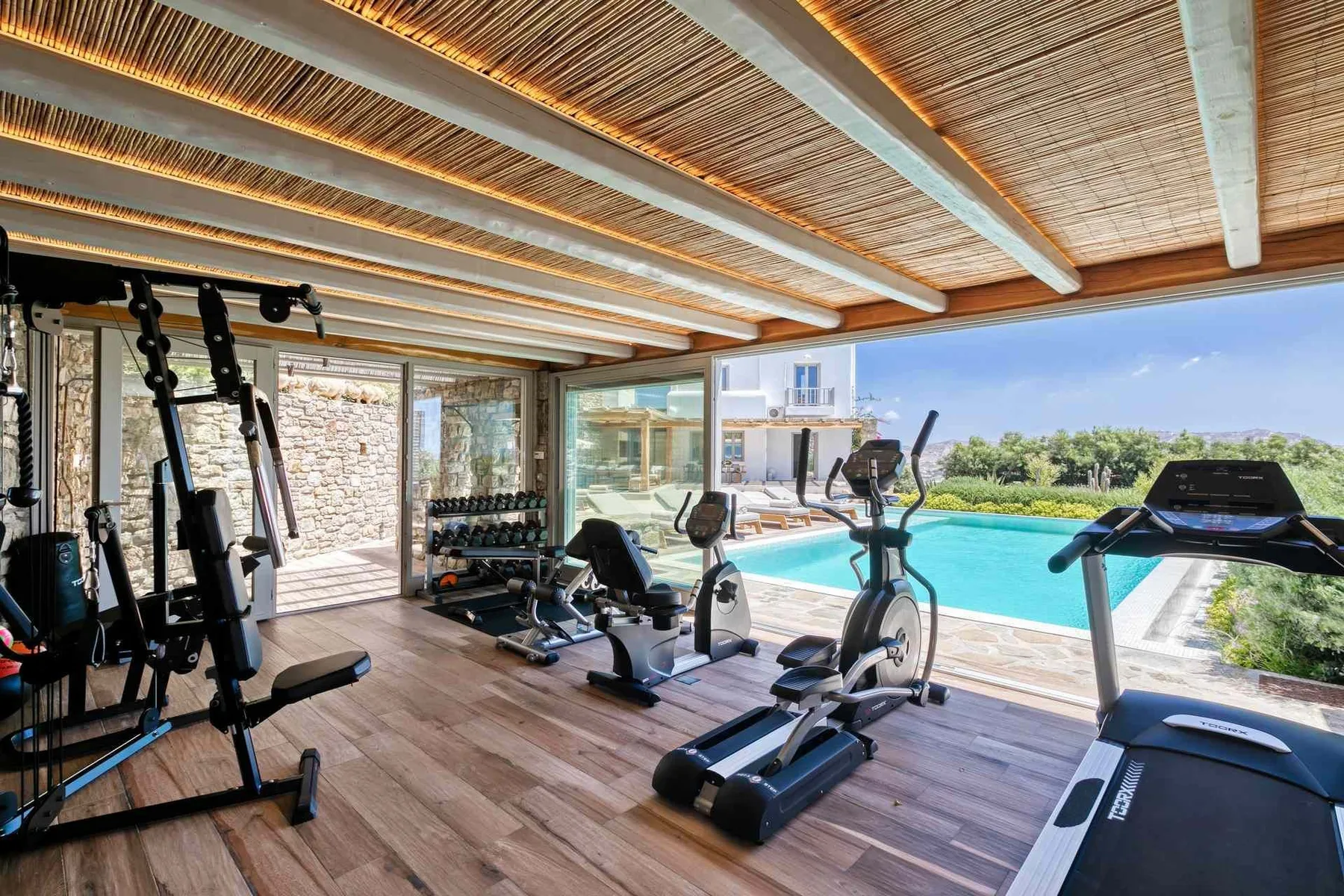 A gym with exercise machines overlooks an outdoor swimming pool.